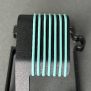 A close-up of a black textured component with eight vertical mint green ribbed bars, set against a neutral gray background.