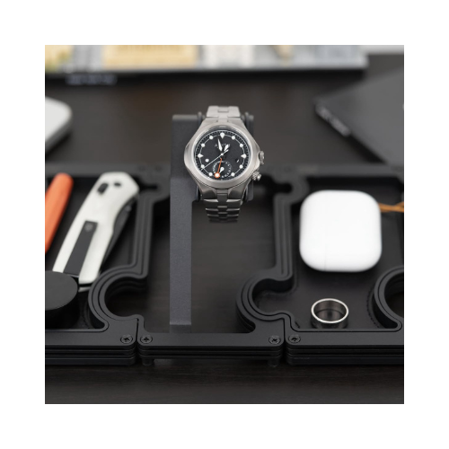 Silver watch on a black stand with various items in the background