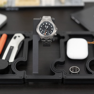 Silver watch on a black stand with various items in the background