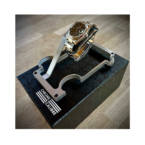 Gold and silver watch on a unique stand with 'Chrome Calibre' branding on a wooden surface.