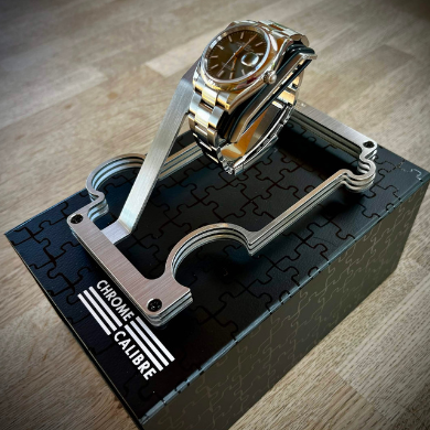 Gold and silver watch on a unique stand with 'Chrome Calibre' branding on a wooden surface.