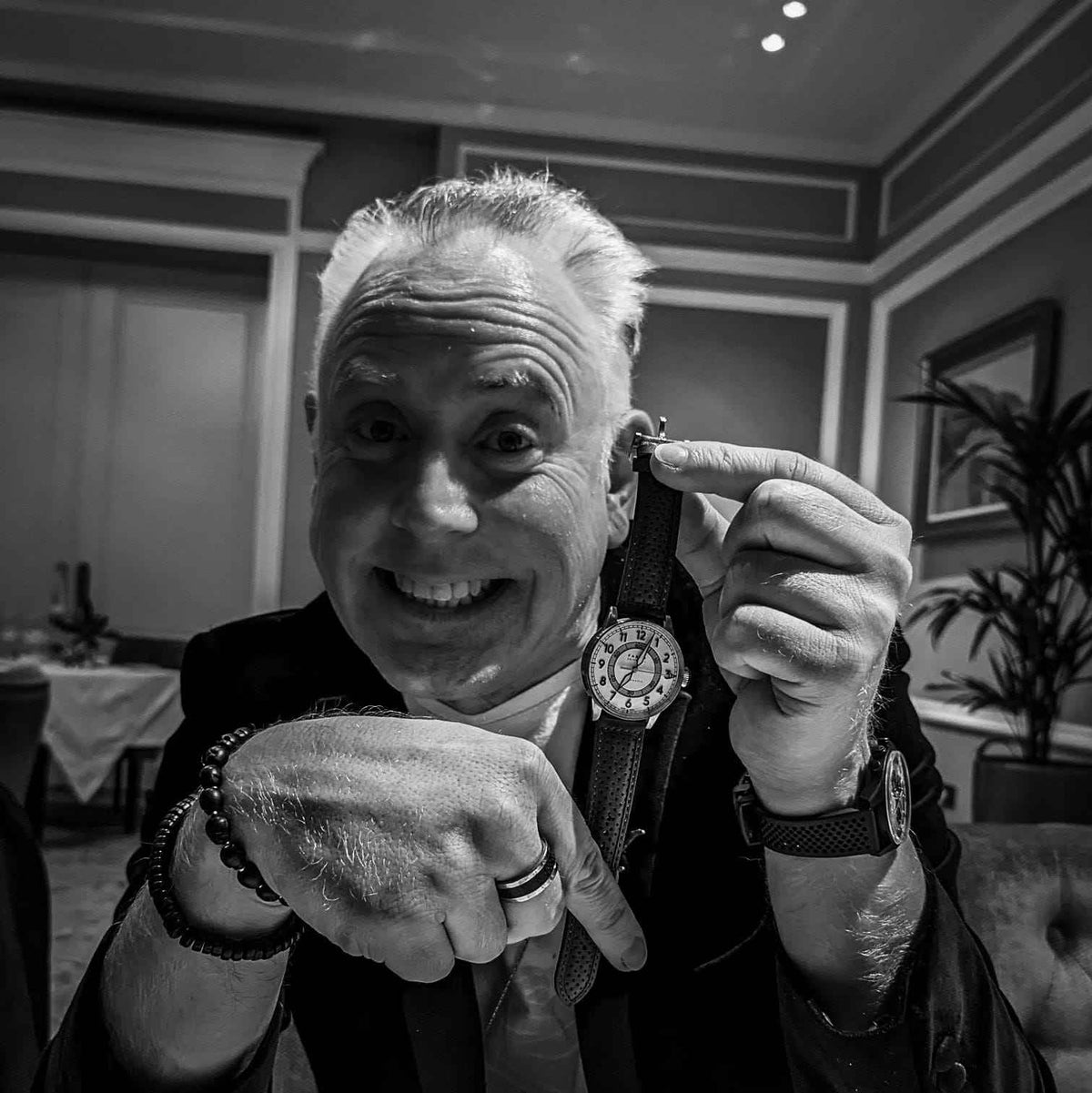 Man adjusting his watch in a formal setting. The image is of Karl Brown and he is holding a white dialed watch and smiling. The tone of the image is black and white
