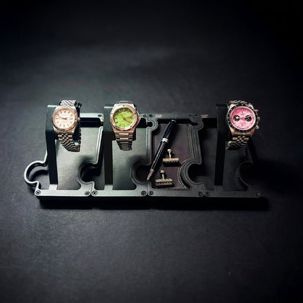 A black watch stand set with three watch slots, shown holding three wristwatches and accessories on a dark background.
