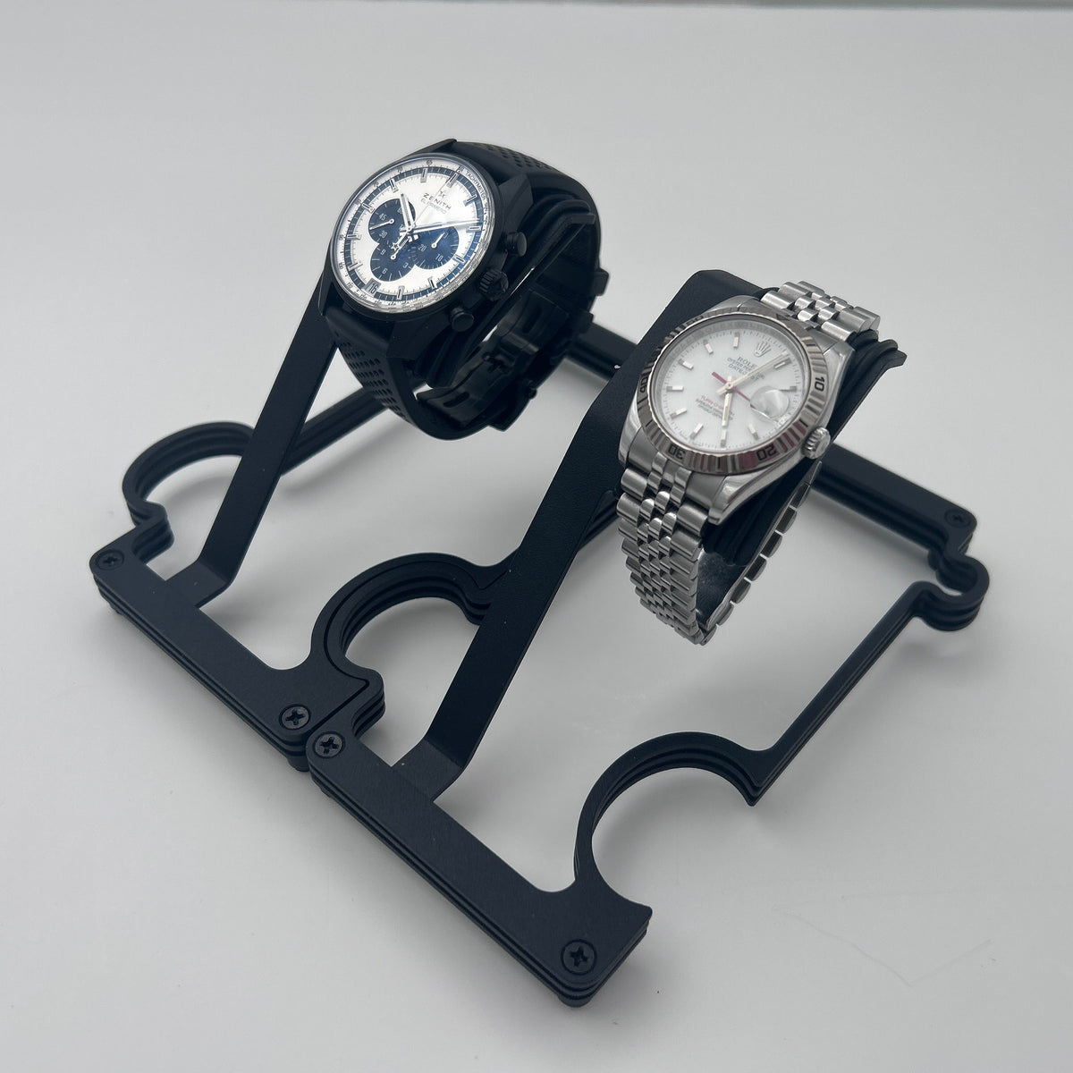 Two wristwatches displayed on a black dual-watch stand against a light gray background.