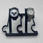 Two wristwatches displayed on a black plastic dual-watch stand against a light gray background.