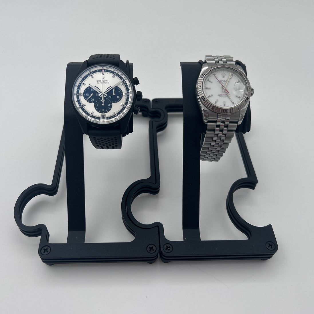 Two wristwatches displayed on a black plastic dual-watch stand against a light gray background.