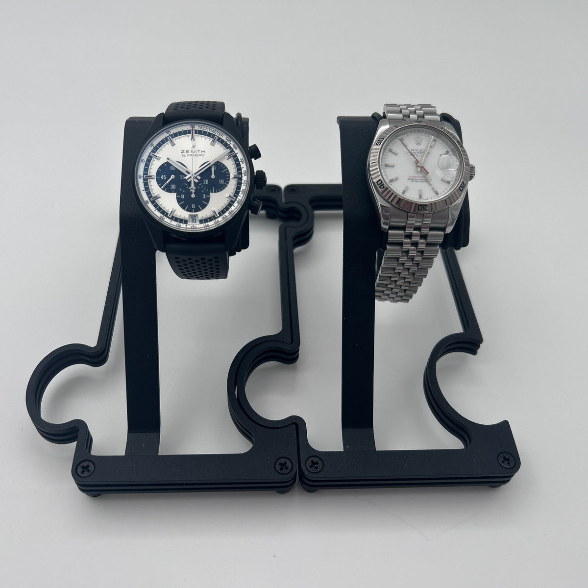 Two wristwatches displayed on a black plastic dual-watch stand against a light gray background.
