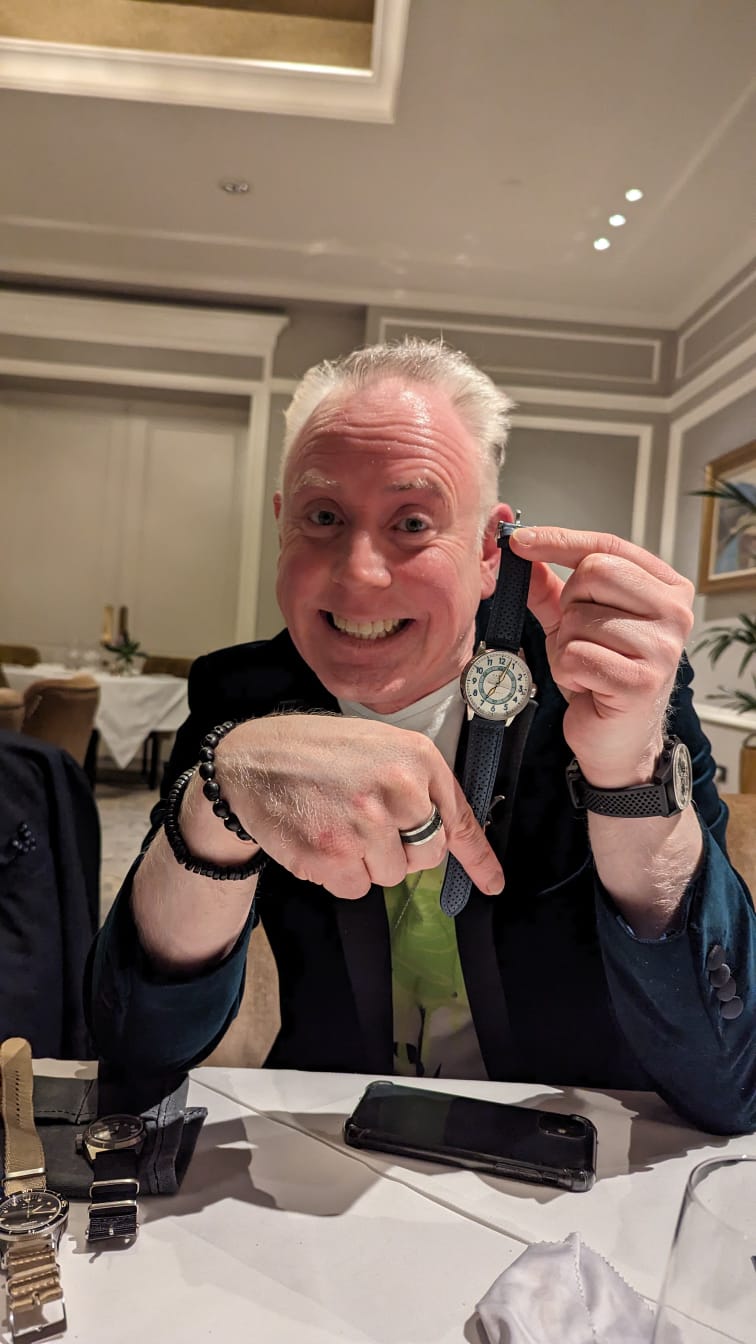 Man sitting at a table in a formal setting, holding a watch