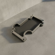 A modern vanity tray in steel with a dark leather insert and a brushed steel metallic frame, resting on a textured concrete background