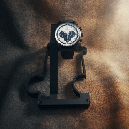 A black chronograph wristwatch with a white dial and black bezel, displayed on a black stand against a textured brown background.