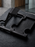 A black metal watch stand and vanity tray  accessorydisplayed on a dark textured stone slab in a modern interior setting.