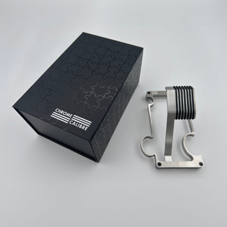 Metallic watch stand next to a black box with 'Chrome Calibre' branding on a light gray background