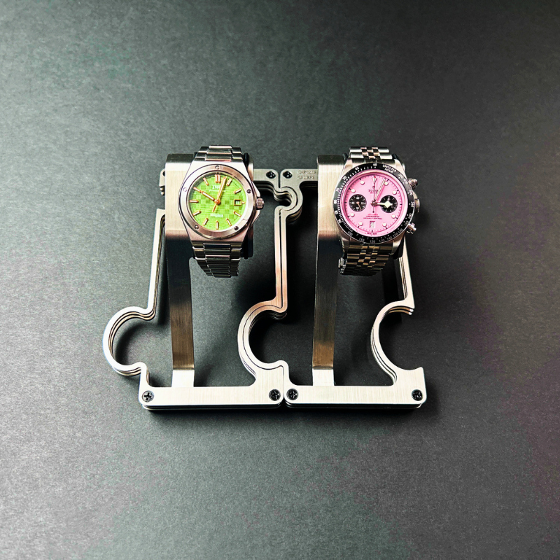Two watches on a metallic stand against a dark background