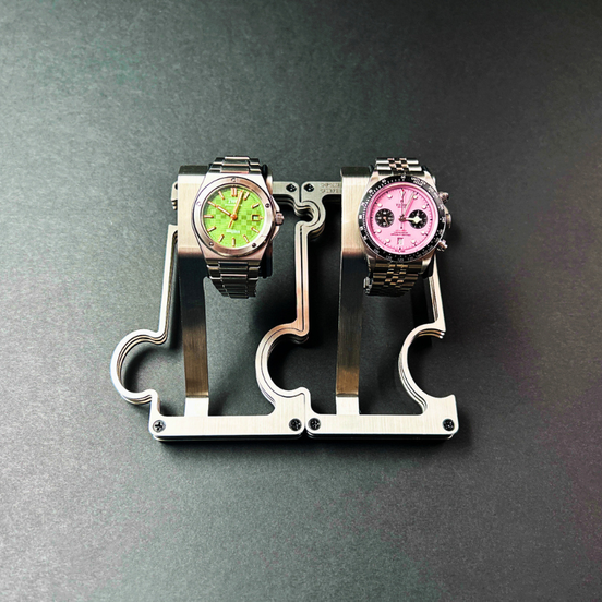 Two watches on a metallic stand against a dark background