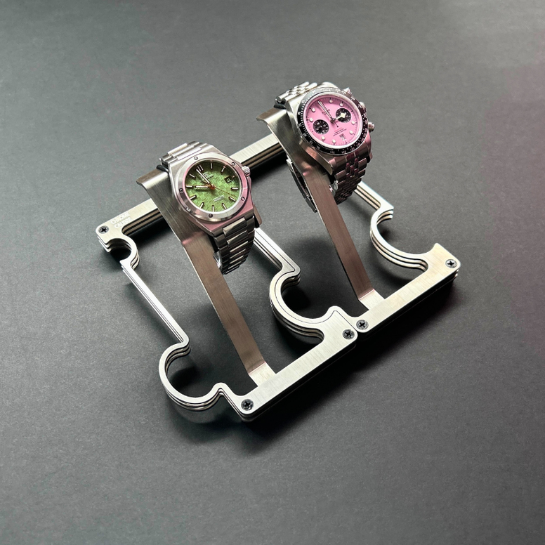Two watches on a metal stand against a gray background