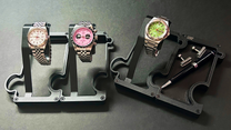 Three watches on display stands against a dark background