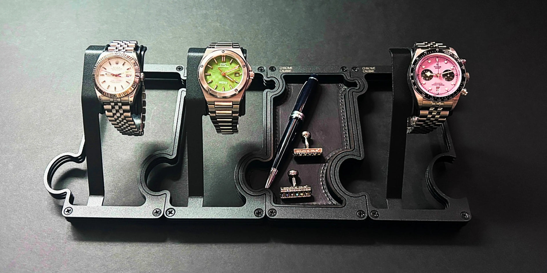 Three watches on a display stand with a pen on a dark background