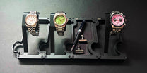 Three watches on a display stand with a pen on a dark background