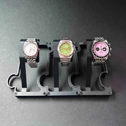 Three watches on a black display stand against a gray background