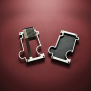 Two metallic objects on a red background. The product on the left of the image is a metal watch stand for wrist watches. The product on the right is a vanity/ valet tray with a leather insert in black. The outline of the products depicts a jigsaw puzzle which allows the products to interlink