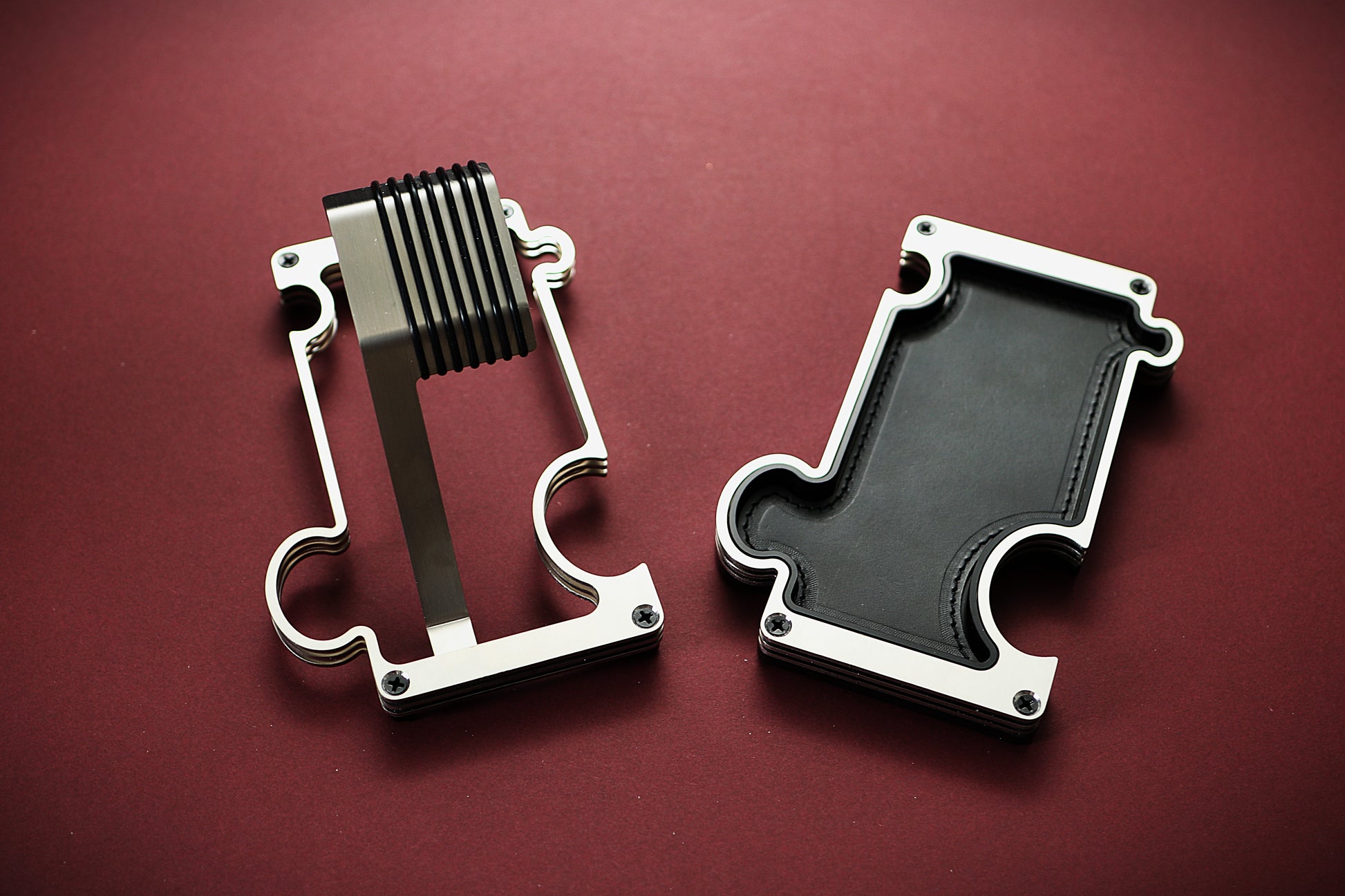 Two metallic objects on a red background. The product on the left of the image is a metal watch stand for wrist watches. The product on the right is a vanity/ valet tray with a leather insert in black. The outline of the products depicts a jigsaw puzzle which allows the products to interlink