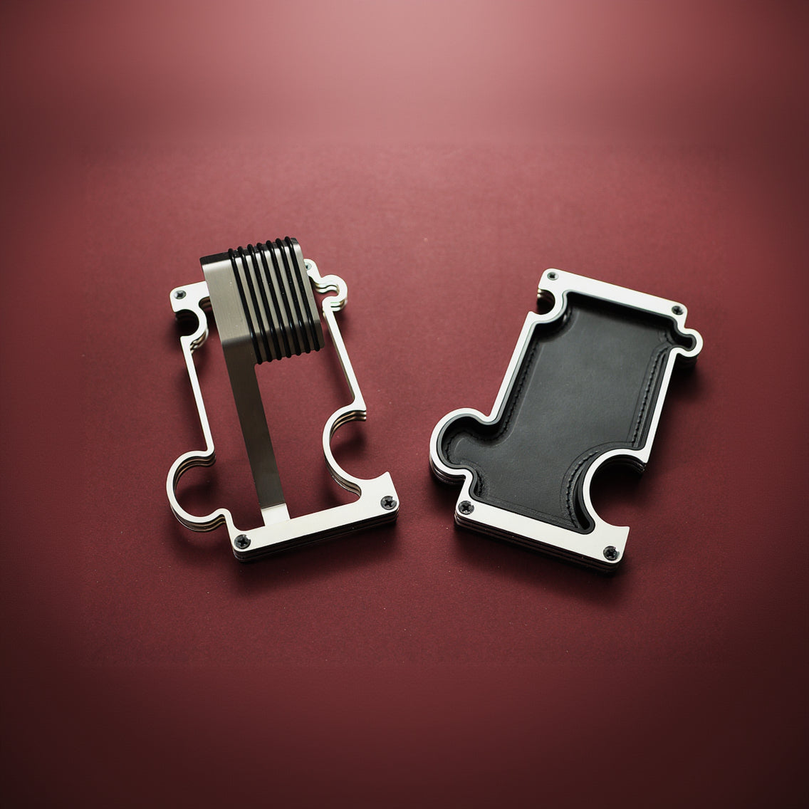 Two metallic objects on a red background. The product on the left of the image is a metal watch stand for wrist watches. The product on the right is a vanity/ valet tray with a leather insert in black. The outline of the products depicts a jigsaw puzzle which allows the products to interlink